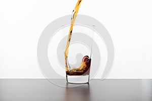 Cola drink pouring into a transparent glass on a wooden table on a white background