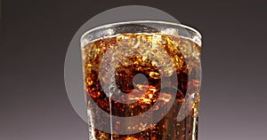 Cola glass with ice cubes slowly rotating close-up. Cold soda drink spinning over brown background. 4K video footage