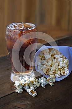 Cola in glass with popcorn on wood background