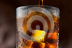 Cola pouring in glass with ice cubes