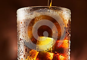 Cola pouring in glass with ice cubes