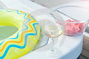 Cold alcohol fruit cocktail beverage in glass near swimming pool with blue clean water