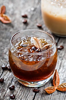 Cold alcoholic cocktail with coffee, cognac and ice in glass on wooden background.