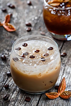 Cold alcoholic cocktail with coffee and ice in glass on wooden background.