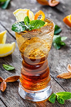 Cold alcoholic cocktail with cola, ice, mint and lemon in glass on wooden background. Summer drinks