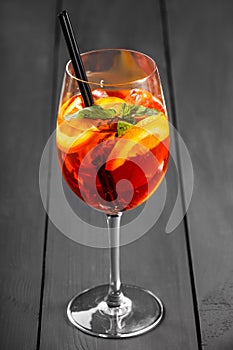 Cold alcoholic cocktail with cola, ice, mint and orange in wineglass on wooden background