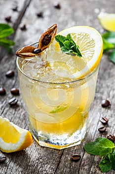 Cold alcoholic cocktail with lemon, lime and mint in glass on wooden background. Summer drinks