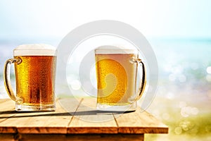 Cold beer in big glass on wooden table with ocean and sandy beach background. Copy space for advertising product.