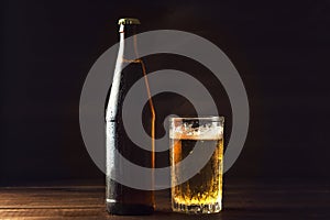 Cold beer bottle and glass with fresh beer in drops of water on dark background, craft brewery