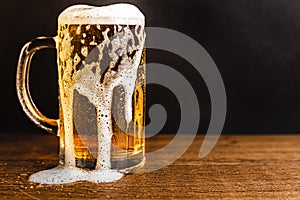 Cold beer with foam in a mug, on a wooden table and a dark background with blank space for a logo or text. Stock Photo mug of cold