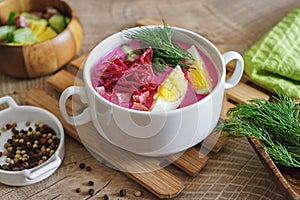 Cold beetroot soup with sausage, egg and vegetables on a rustic wooden table