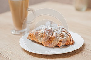 Cold black coffee with ice cubes in tall glass and fresh croissant.