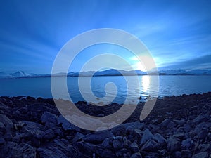 Cold blue fjord and snowy mountain landscape with sunset