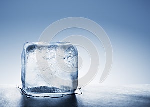 Cold blue ice block melting into water puddle