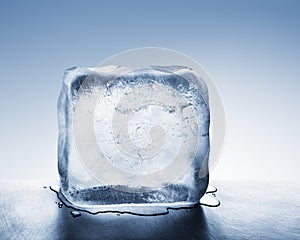 Cold blue ice block melting into water puddle