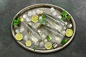 Cold bottled water with ice cubes, lime slices and mint leaves on a metal tray. Summer refreshing drink. Flat lay, overhead
