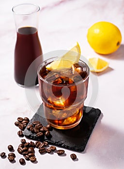 Cold brew coffee in a glass with ice and lemon on a light marble background with coffee beans and bottle. Concept summer craft