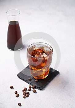Cold brew coffee in a glass with ice on a light background with coffee beans and bottle. Concept summer craft refreshing homemade