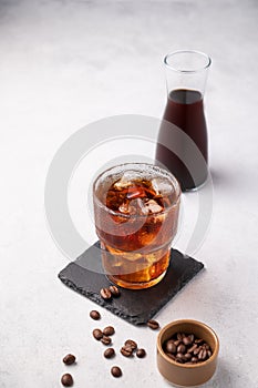 Cold brew coffee in a glass with ice on a light background with coffee beans and bottle. Concept summer craft refreshing homemade