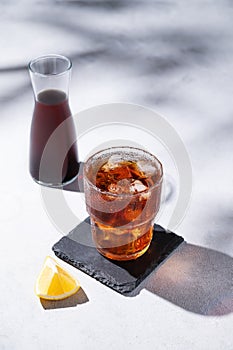 Cold brew coffee in a glass with ice on a light background with lemon fruit, bottle and shadows. Concept summer craft refreshing