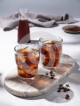 Cold brew coffee in a two glasses with ice on a marble board on a light background with coffee beans, bottle and napkin. Concept