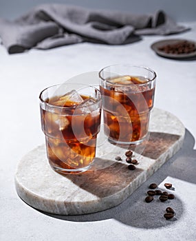 Cold brew coffee in a two glasses with ice on a marble board on a light background with coffee beans, shadows and napkin. Concept
