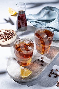 Cold brew coffee in a two glasses with lemon and ice on a marble board on a light background with coffee beans, bottle and shadows