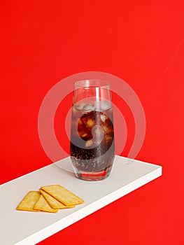 Cold carbonated drink with ice cubes and Cracker Biscuit isolated on red background