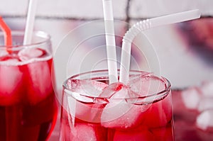 Cold cherry drink with ice cubes and cocktail tubes in glasses, on pink background