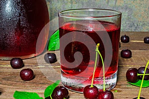 Cold cherry juice in a glass and pitcher on wooden table with ripe berries around