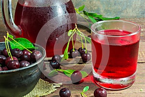 Cold cherry juice in a glass and pitcher on wooden table with ripe berries in pottery bowl