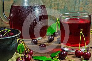 Cold cherry juice in a glass and pitcher on wooden table with ripe berries in pottery bowl