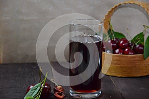 Cold cherry juice in a glass and pitcher on wooden table with ripe berries in wicker basket