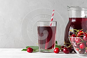 Cold cherry juice in a glass with a straw and jug with fresh berries on white background. Refreshment summer drink