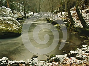 Cold clear water of mountain river in winter time, icicles on boulder