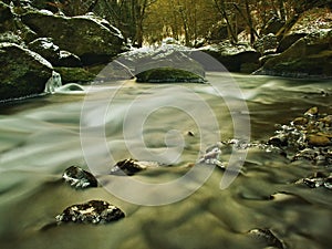 Cold clear water of mountain river in winter time, icicles on boulder