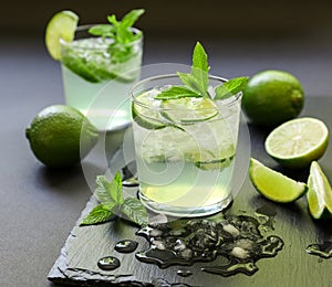 Cold cocktail with lemon liqueur, lime, tonic, ice on dark background.