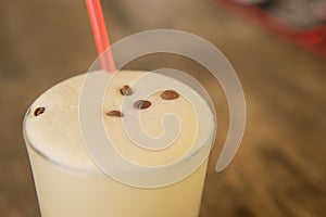 A cold coffee cocktail in a clear glass with a straw on a wooden bar counter