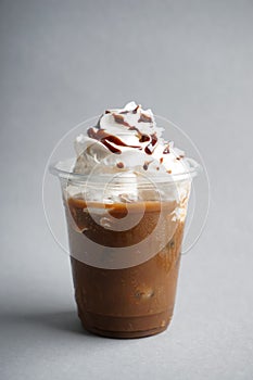 Cold coffee covered with whipped cream and chocolate in wet plastic cup on light background