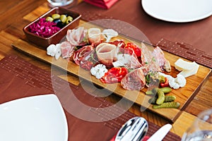 Cold cuts on wooden board with prosciutto, bacon, salami and sausages. Meat platter appetizers served with pickle and olives.