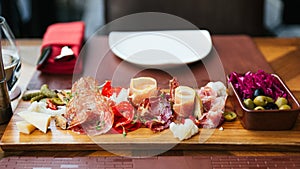 Cold cuts on wooden board with prosciutto, bacon, salami and sausages. Meat platter appetizers served with pickle and olives.