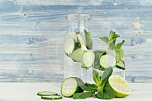 Cold detox water in glass and retro bottle with slices cucumber, mint, lime and straw on shabby light blue wood board.