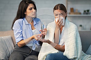 Girl Giving Pills And Water To Friend Sitting On Sofa