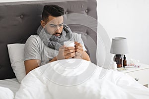 Cold And Flu. Portrait Of Sick Arab Man Drinking Tea In Bed