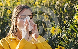 Cold flu season, runny nose. Flowering trees in background. Young girl sneezing and holding paper tissue in one hand and