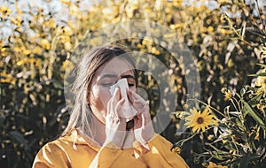 Cold flu season, runny nose. Flowering trees in background. Young girl sneezing and holding paper tissue in one hand and