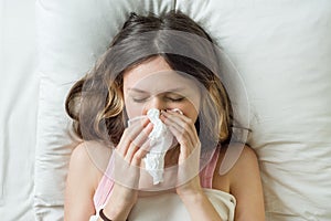 Cold flu season, runny nose. Sick girl on bed sneezing in handkerchief in bedroom