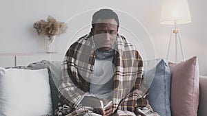 Cold and flu symptoms. Young african american man suffering from influenza, sneezing and blowing nose at home