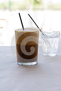 Cold frappe coffee with ice cubes on glass with black straw served on the table in caffeteria