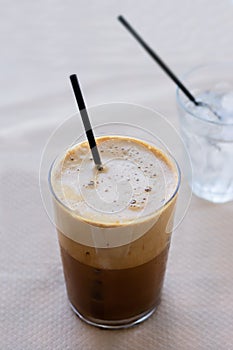 Cold frappe coffee with ice cubes on glass with black straw served on the table in caffeteria.